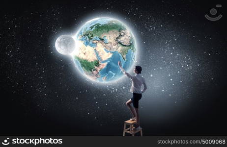 Businesswoman reaching planet in sky. Businesswoman standing on chair and reaching Earth planet. Elements of this image are furnished by NASA