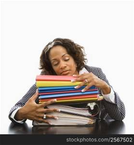Businesswoman resting head on large stack of books and files with eyes closed.