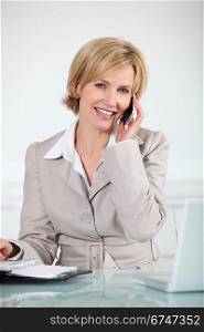 Businesswoman sat at desk holding mobile telephone