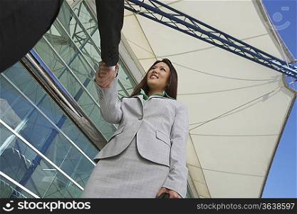 Businesswoman shaking hands with businessman outdoors, low angle view