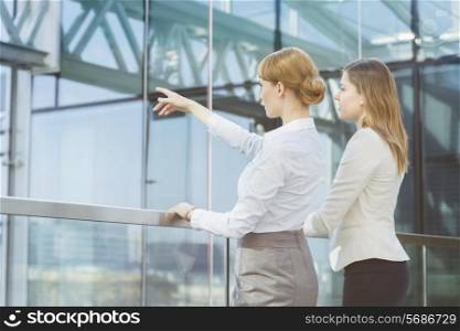 Businesswoman showing something to female colleague from glass wall in office