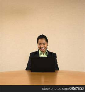 Businesswoman sitting at conference table smiling and typing on laptop computer.