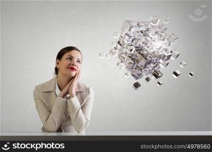 Businesswoman sitting at desk. Happy attractive businesswoman sitting at table in office and 3D rendering cube figure