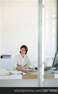 Businesswoman sitting at desk in office front view.