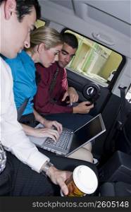 Businesswoman sitting between two businessmen and using a laptop in a car