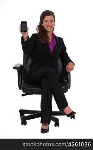 Businesswoman sitting in a swivel chair and holding up a mobile phone