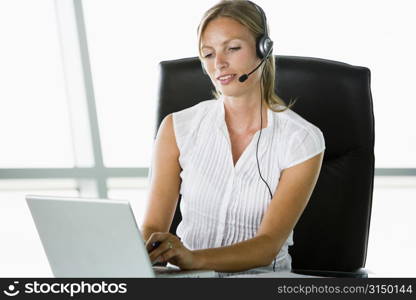 Businesswoman sitting in office wearing headset using laptop