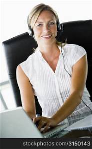 Businesswoman sitting in office wearing headset using laptop and smiling