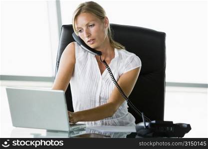 Businesswoman sitting in office with laptop on telephone