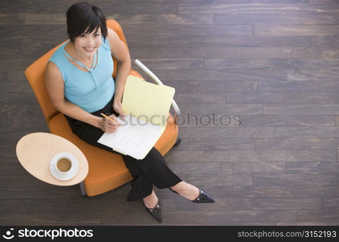 Businesswoman sitting indoors with coffee and folder smiling