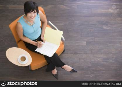 Businesswoman sitting indoors with coffee and folder smiling