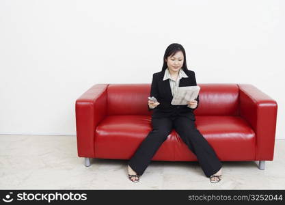 Businesswoman sitting on a couch holding a newspaper and a mobile phone