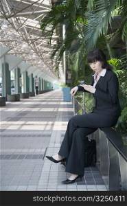 Businesswoman sitting on a railing and using a mobile phone