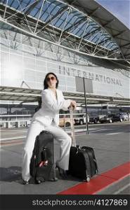 Businesswoman sitting on a suitcase and waiting for a taxi outside an airport