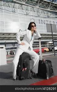 Businesswoman sitting on a suitcase and waiting for a taxi outside an airport