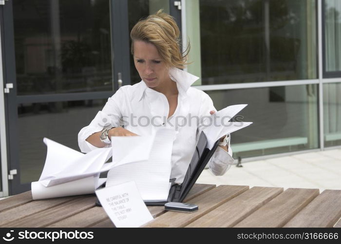 Businesswoman sitting outdoors with her notes and trying to control the paper blowing in the wind