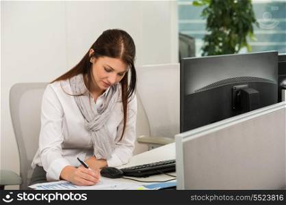 Businesswoman sitting while writing at computer desk