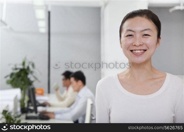 Businesswoman smiling in the office, coworkers in the background