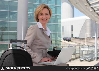 Businesswoman smiling on laptop outside airport