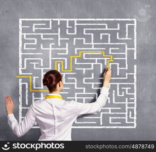 Businesswoman solving maze problem. Back view image of young businesswoman trying to find way in labyrinth