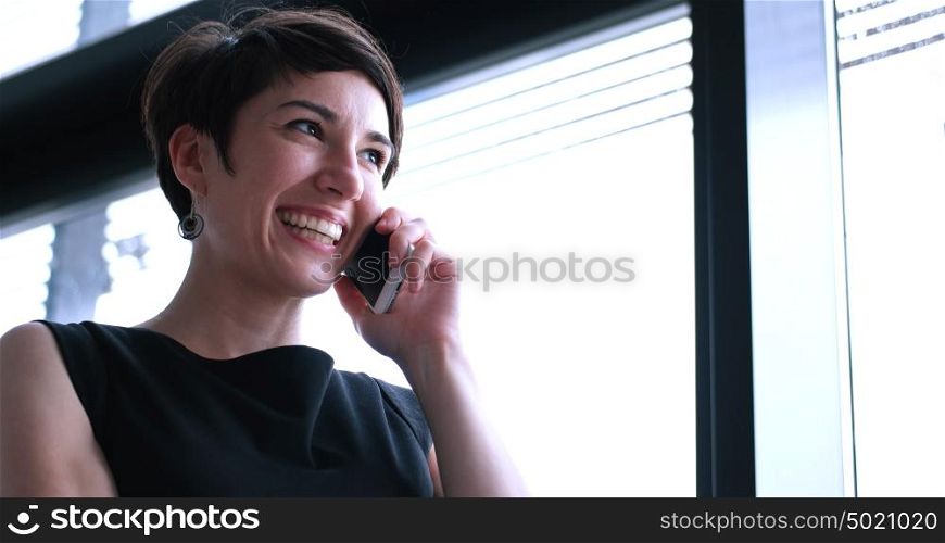 businesswoman speeking on phone beside window of modern office