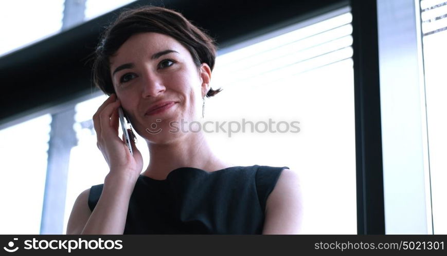 businesswoman speeking on phone beside window of modern office