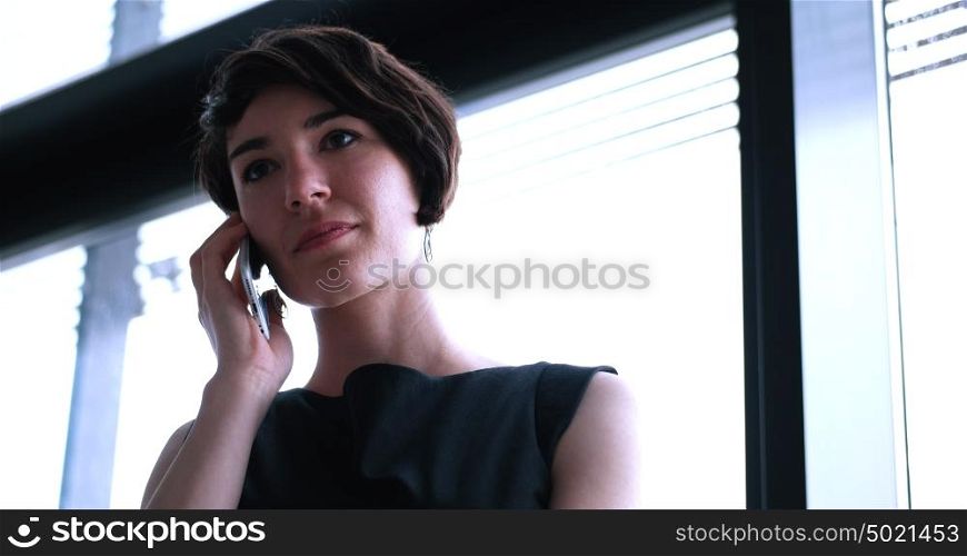 businesswoman speeking on phone beside window of modern office
