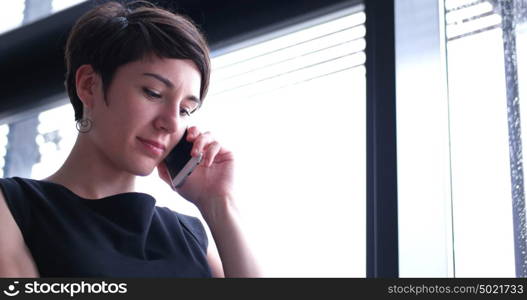 businesswoman speeking on phone beside window of modern office