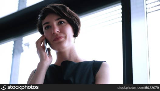 businesswoman speeking on phone beside window of modern office