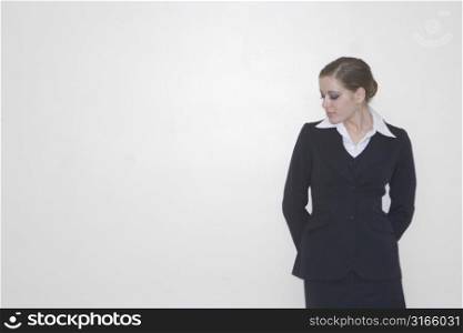 Businesswoman standing against a white wall in her business suit looking down
