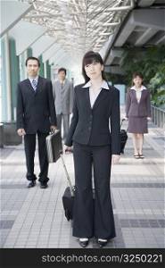 Businesswoman standing and holding his luggage with three business executives in the background