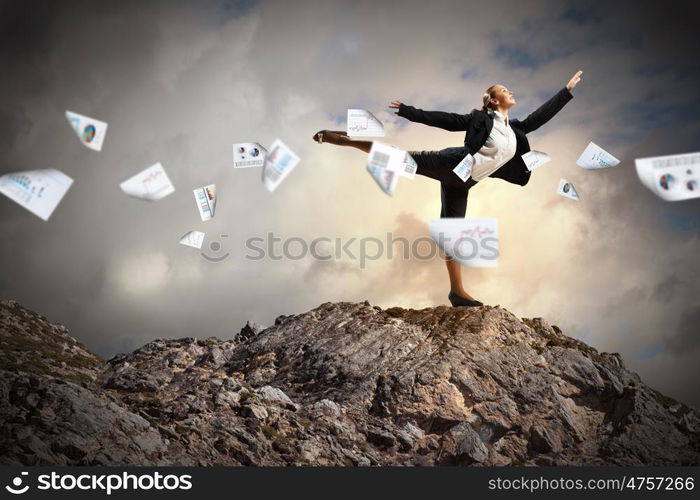 businesswoman standing atop of mountain. young businesswoman standing on one leg atop of mountain against diagram background