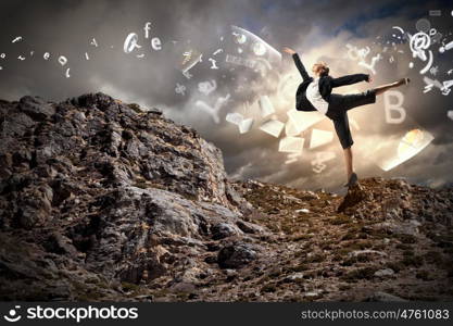 businesswoman standing atop of mountain. young businesswoman standing on one leg atop of mountain against diagram background