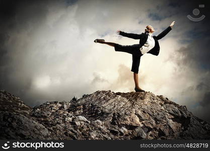 businesswoman standing atop of mountain. young businesswoman standing on one leg atop of mountain against diagram background