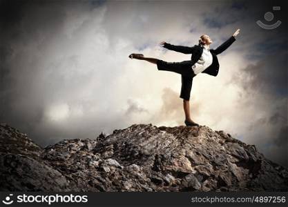businesswoman standing atop of mountain. young businesswoman standing on one leg atop of mountain against diagram background