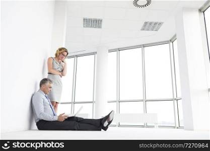 Businesswoman standing by businessman using laptop at new office