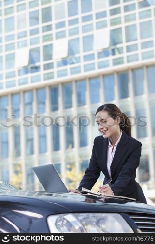 Businesswoman Standing by Car Using Laptop and Writing