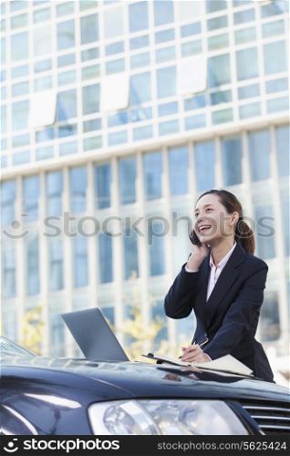 Businesswoman Standing by Car Using Phone and Laptop