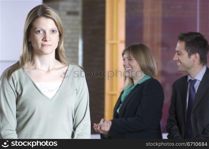 Businesswoman standing in an office with two business executives smiling in the background