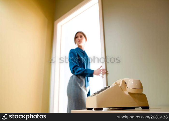 Businesswoman standing in illuminated doorway looking backwards with an expression of concern, telephone in foreground.