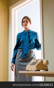 Businesswoman standing in illuminated doorway looking down at telephone in foreground.