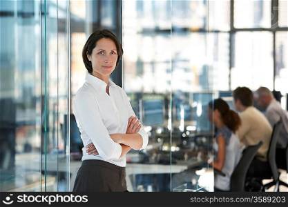 Businesswoman standing in office with group of office workers in background.