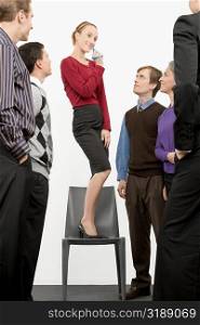 Businesswoman standing on a chair and blowing whistle with business executives standing beside her