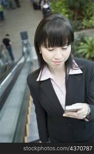 Businesswoman standing on an escalator and looking at a mobile phone