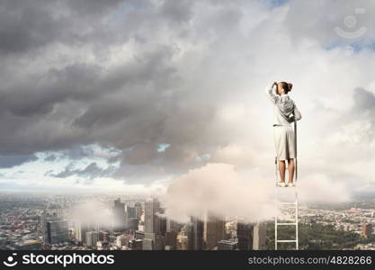 Businesswoman standing on ladder. Businesswoman standing on ladder looking into distance against city background