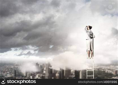 Businesswoman standing on ladder. Businesswoman standing on ladder looking into distance against city background