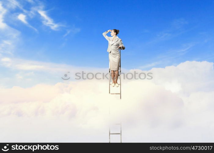 Businesswoman standing on ladder. Businesswoman standing on ladder looking into distance against cloudy background