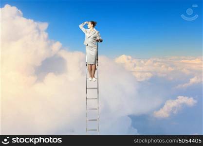 Businesswoman standing on ladder. Businesswoman standing on ladder looking into distance against cloudy background