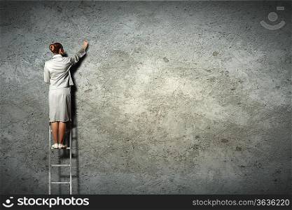 businesswoman standing on ladder drawing diagrams and graphs on wall
