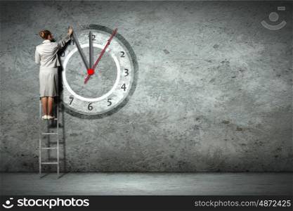 Businesswoman standing on ladder moving hands of clock. Business woman on ladder